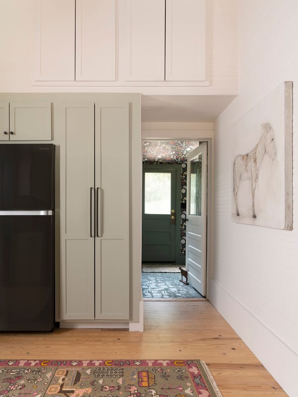 A white kitchen looking through to a green back door, with a plaster horse on the wall.